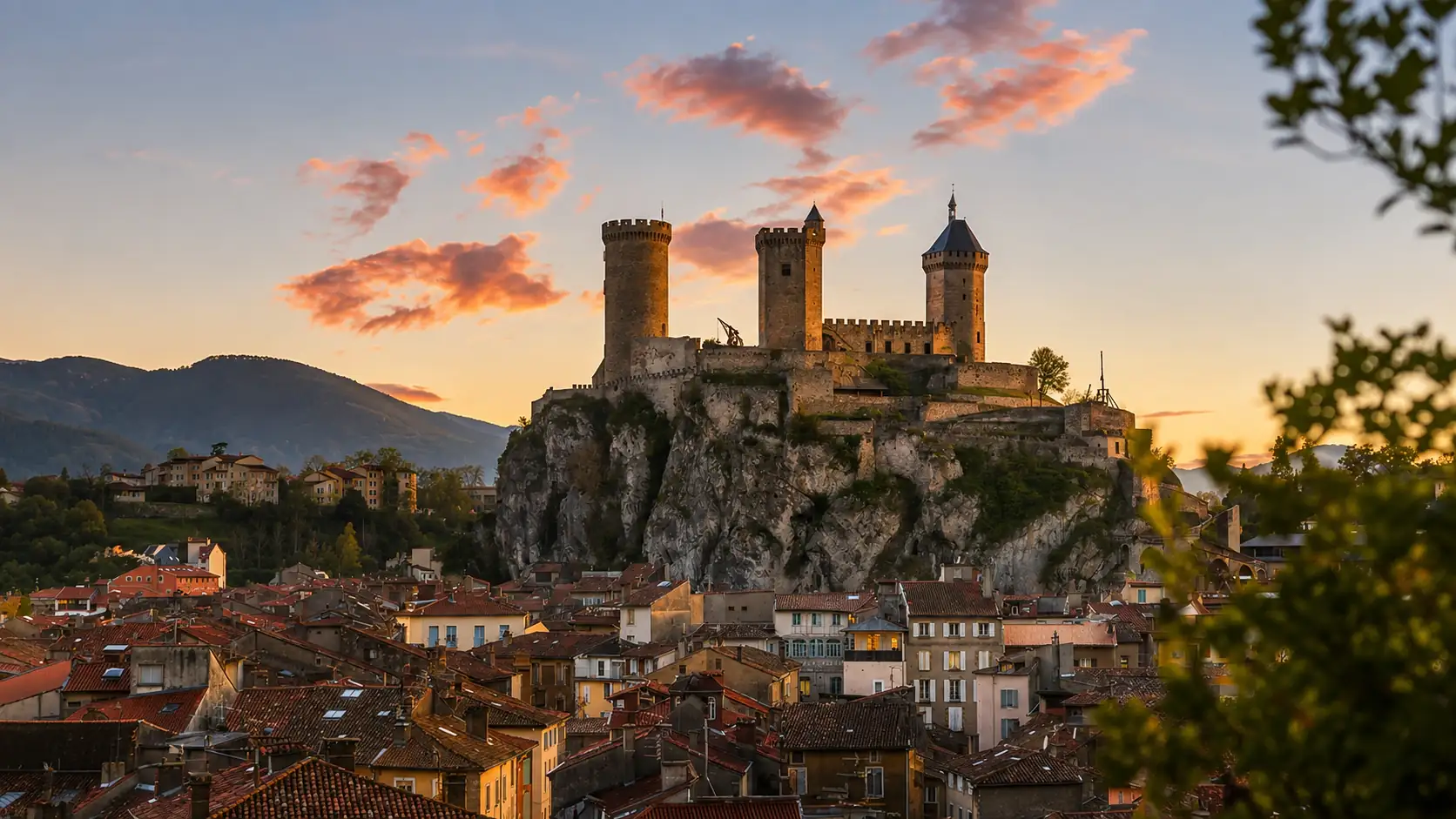 Le château de Foix et ses trois tours dressés sur leur piton rocheux au-dessus des toits de la ville, les reliefs pyrénéens à l'horizon