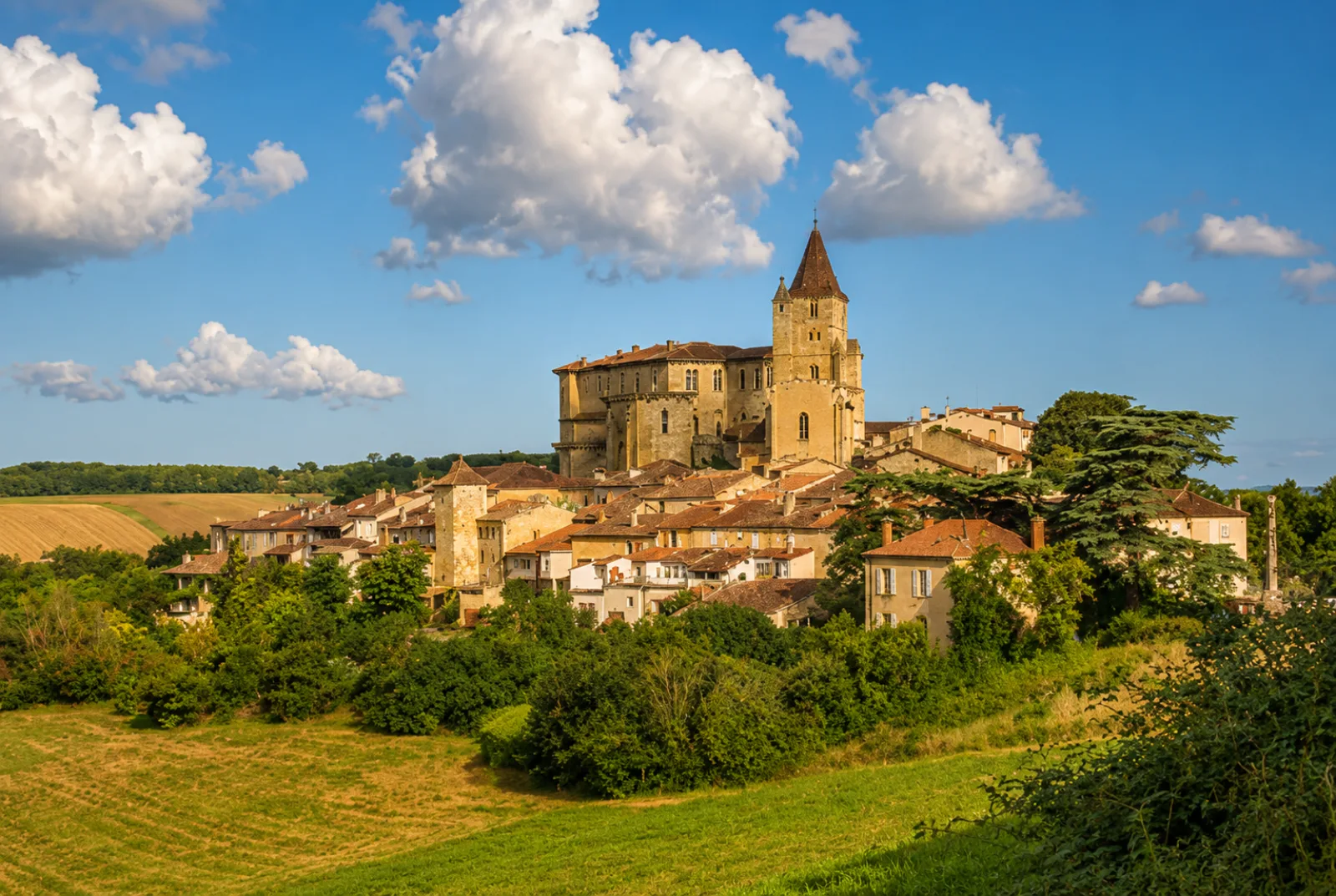 Un village perché du Gers dominé par son château et son clocher — les coteaux de Gascogne et leurs champs moissonnés en contrebas