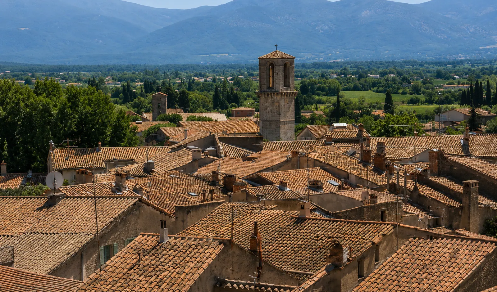 La tour hexagonale du Luc au-dessus des toits de tuiles du village — la plaine des Maures et le massif à l'horizon, en cœur de Provence verte