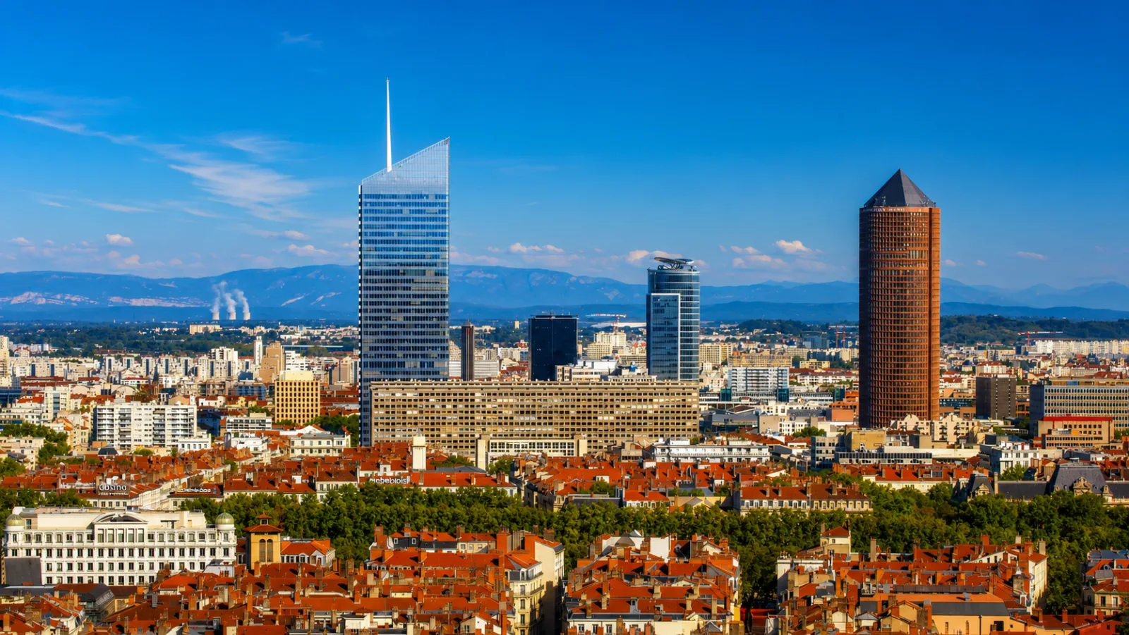 La skyline de la Part-Dieu au-dessus des toits lyonnais — des tours ancrées profond dans les alluvions du Rhône, les reliefs à l'horizon