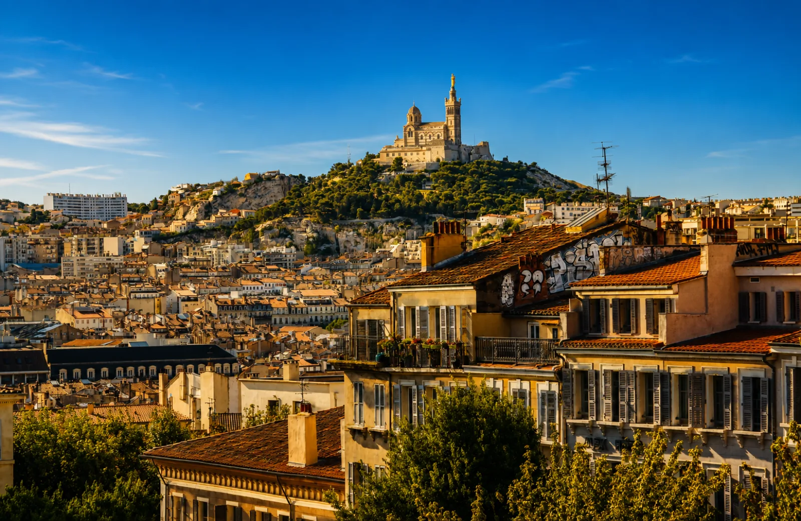 Notre-Dame de la Garde sur son piton calcaire, affleurements à nu au-dessus des toits — Marseille, ville ancienne serrée au pied de ses collines