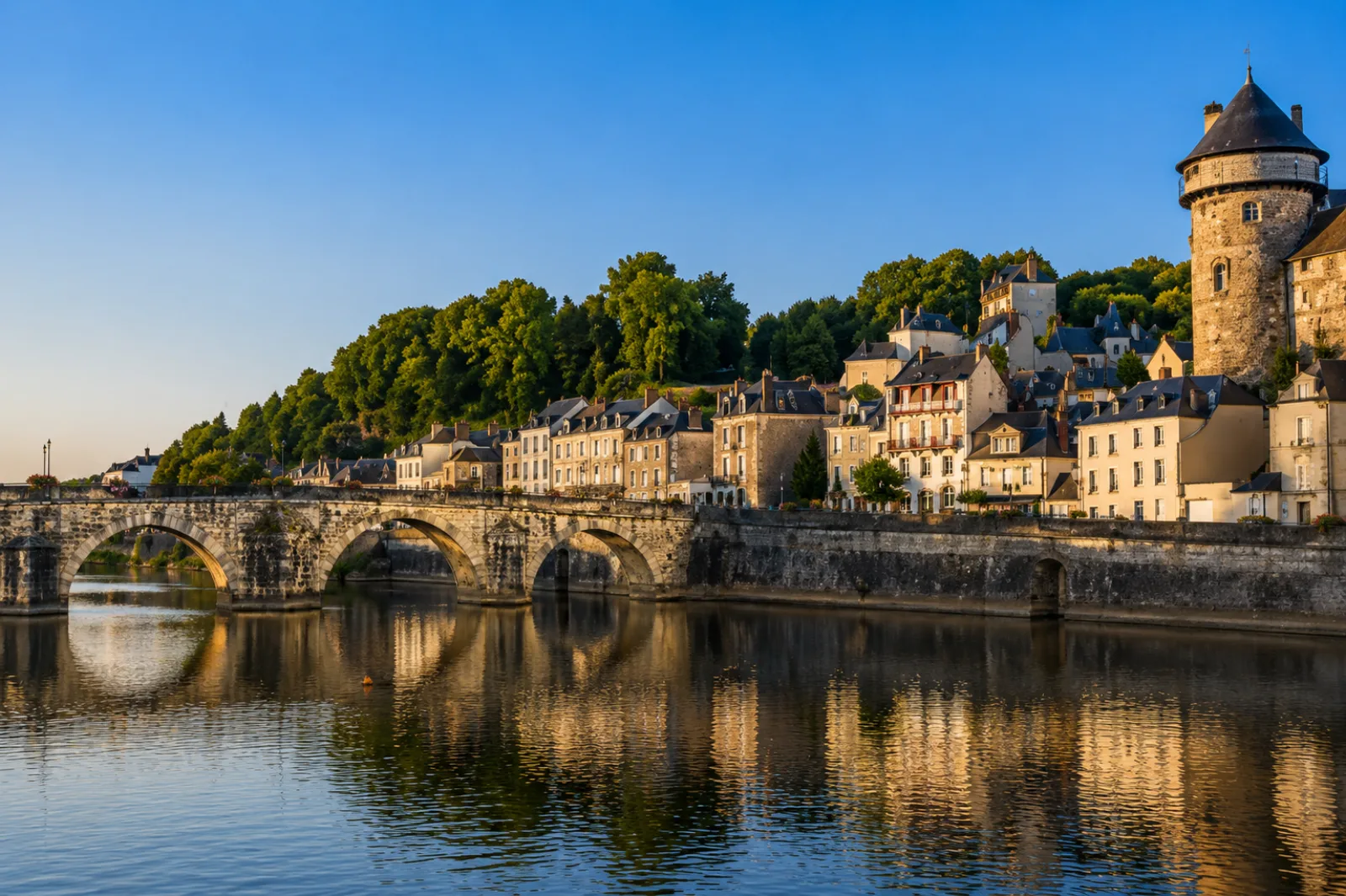 Pont de pierre à arches sur la rivière, tour médiévale et maisons anciennes en surplomb — en Mayenne, on bâtit au bord de l'eau depuis des siècles