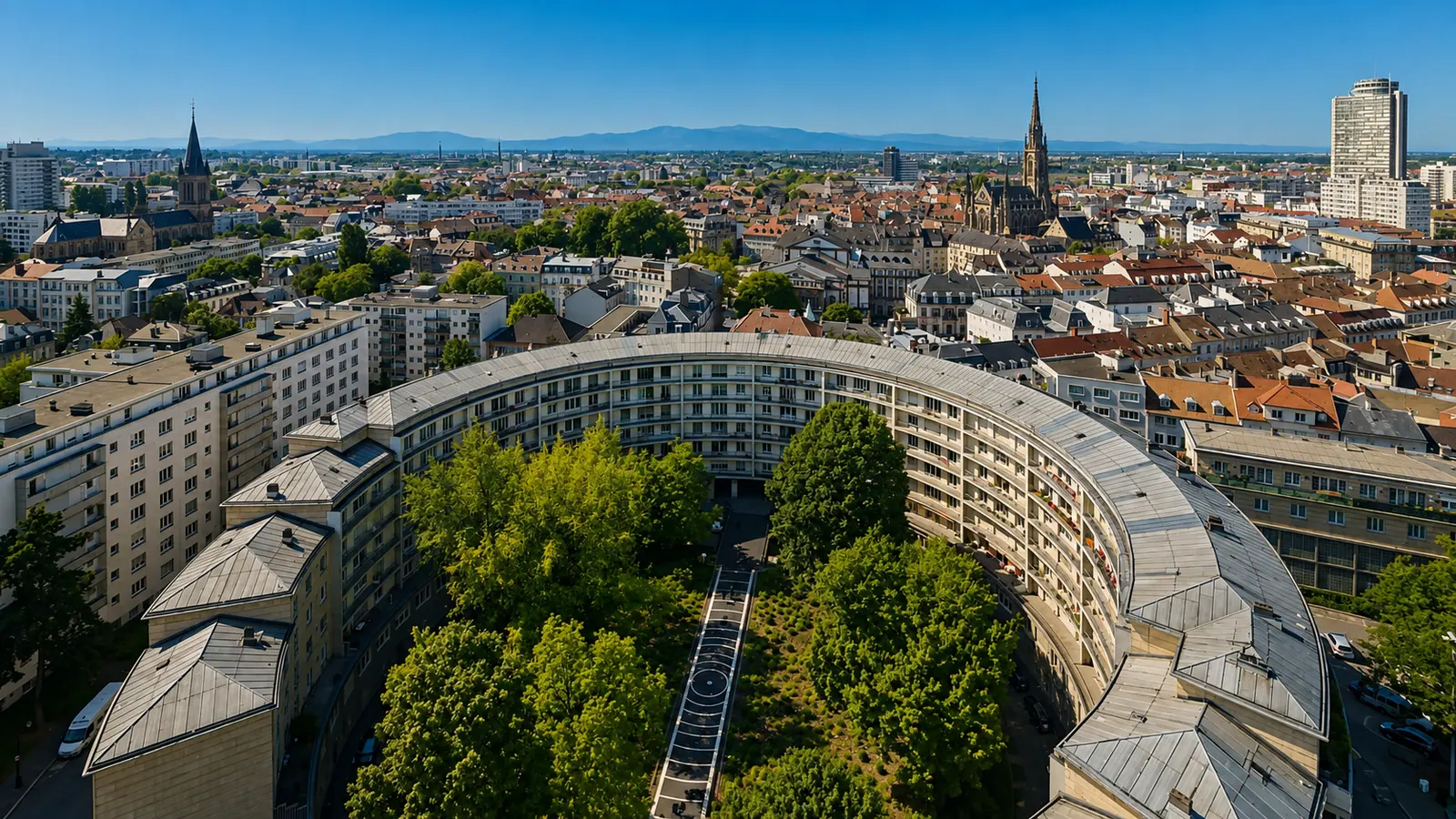Mulhouse vue du ciel — la barre courbe de la Cité et la flèche du temple Saint-Étienne au-dessus des toits, la plaine et les reliefs à l'horizon