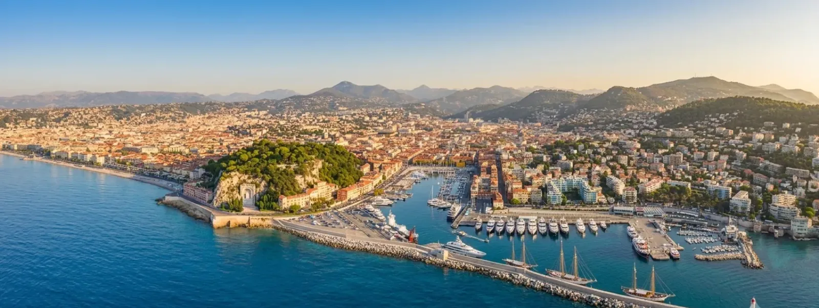Vue aérienne de Nice — la colline du Château entre le port Lympia et la baie des Anges, une ville dense adossée à ses collines