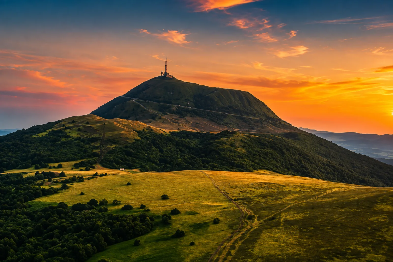 Le puy de Dôme au couchant, son antenne en sentinelle au-dessus des estives — bâtir ici, c'est composer avec les volcans de la chaîne des Puys