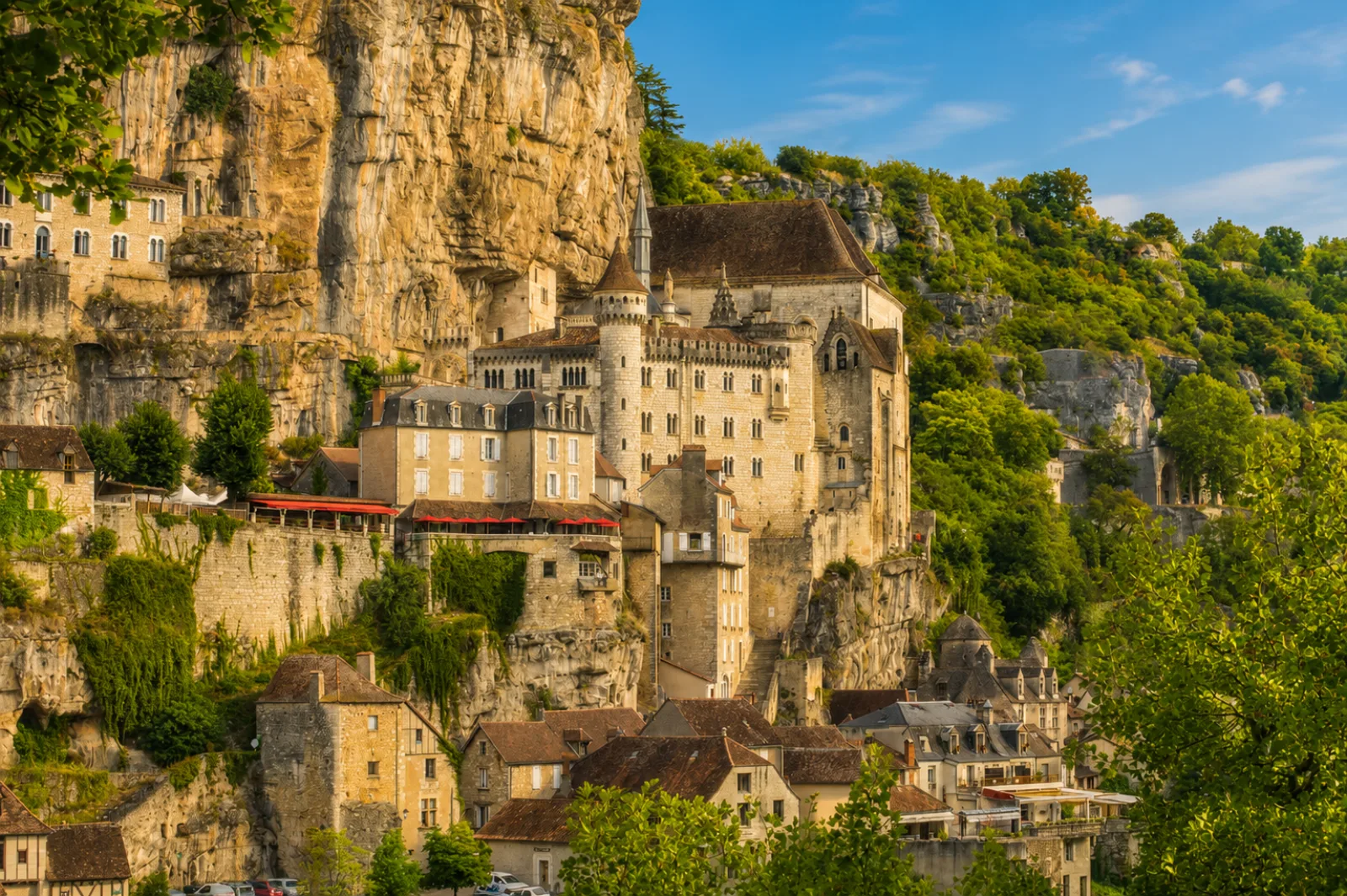 Rocamadour agrippée à sa falaise calcaire — sanctuaires et maisons étagés sous un surplomb rocheux, au-dessus du canyon de l'Alzou