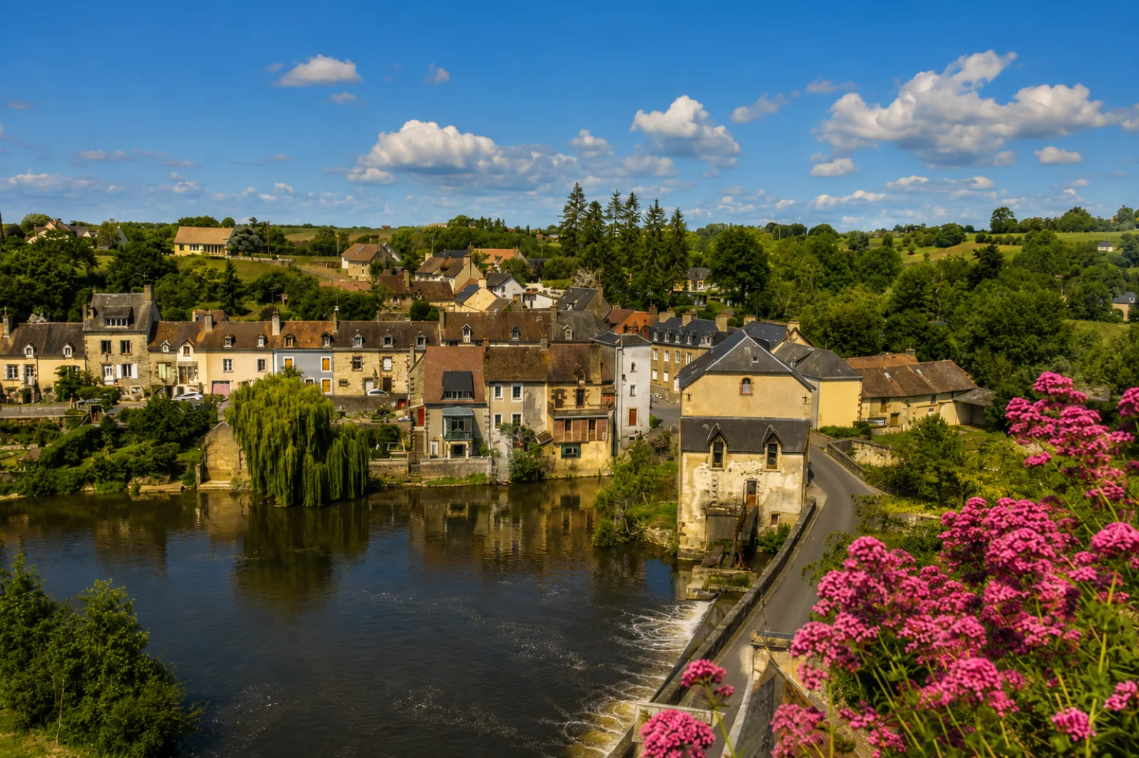 Un bourg sarthois au fil de l'eau — moulin, déversoir et maisons anciennes serrées sur la berge, entre bocage et vallée