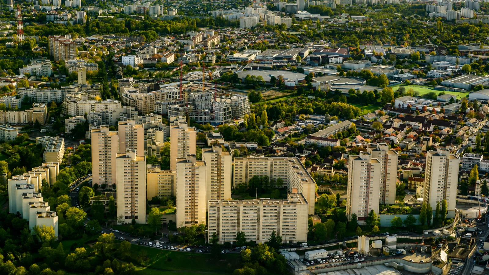 Vue aérienne d'un secteur de Seine-Saint-Denis au couchant — tours et barres, pavillonnaire et zones d'activité imbriqués, grues de renouvellement urbain au milieu
