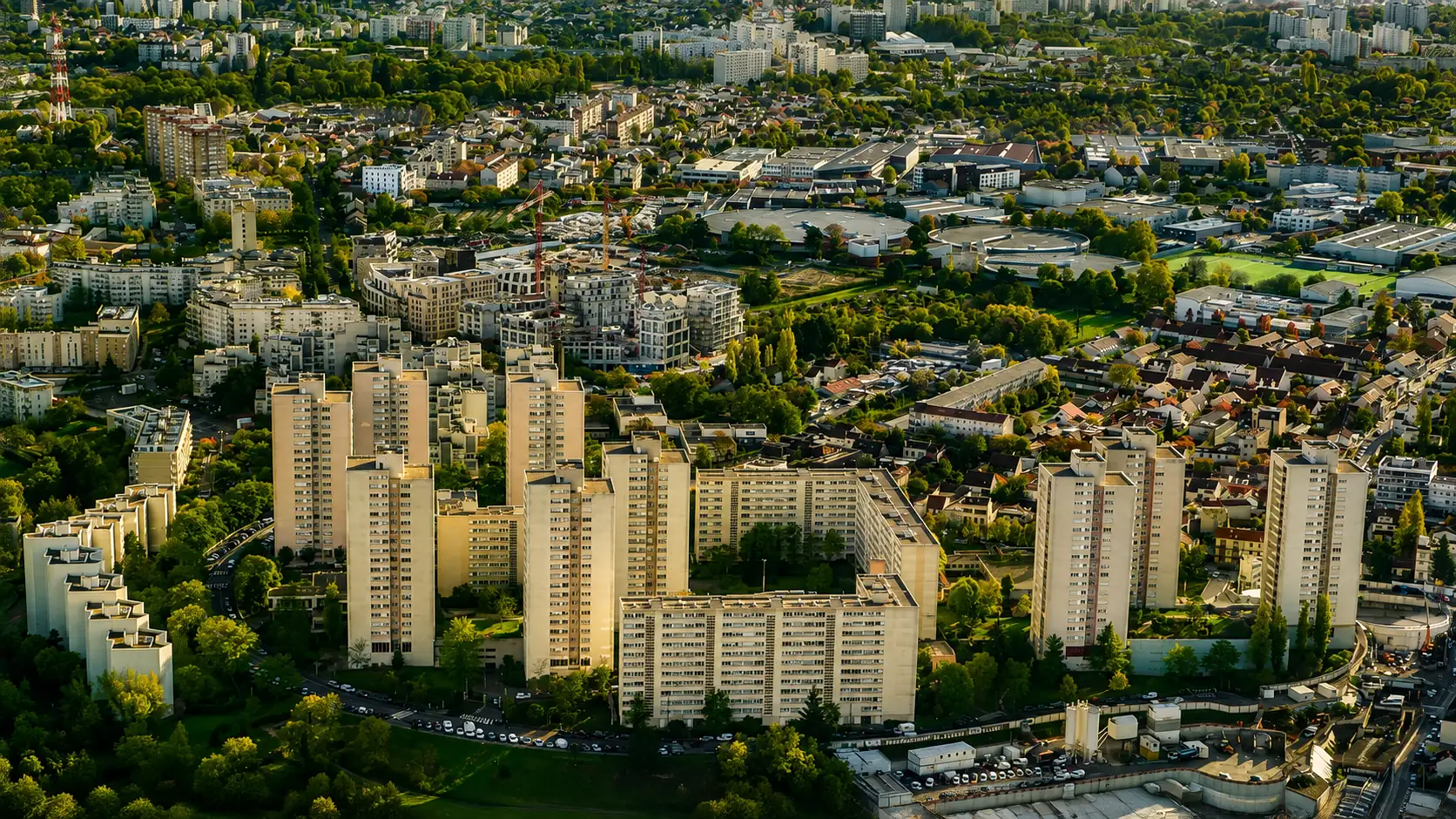 Vue aérienne d'un secteur de Seine-Saint-Denis au couchant — tours et barres, pavillonnaire et zones d'activité imbriqués, grues de renouvellement urbain au milieu